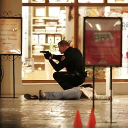 A Salt Lake City Police officer squats with his gun drawn next to a body inside the Trolley Square Mall Monday night. Six people, including the gunman, died from the shooting. (Mike Terry, Deseret Morning News)